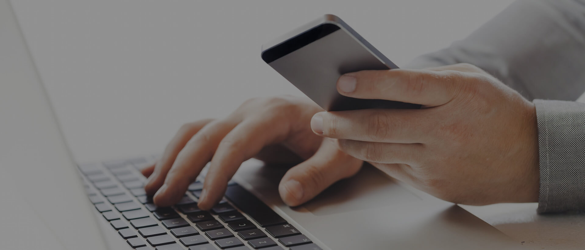 A man's hand resting on a keyboard and holding a mobile phone